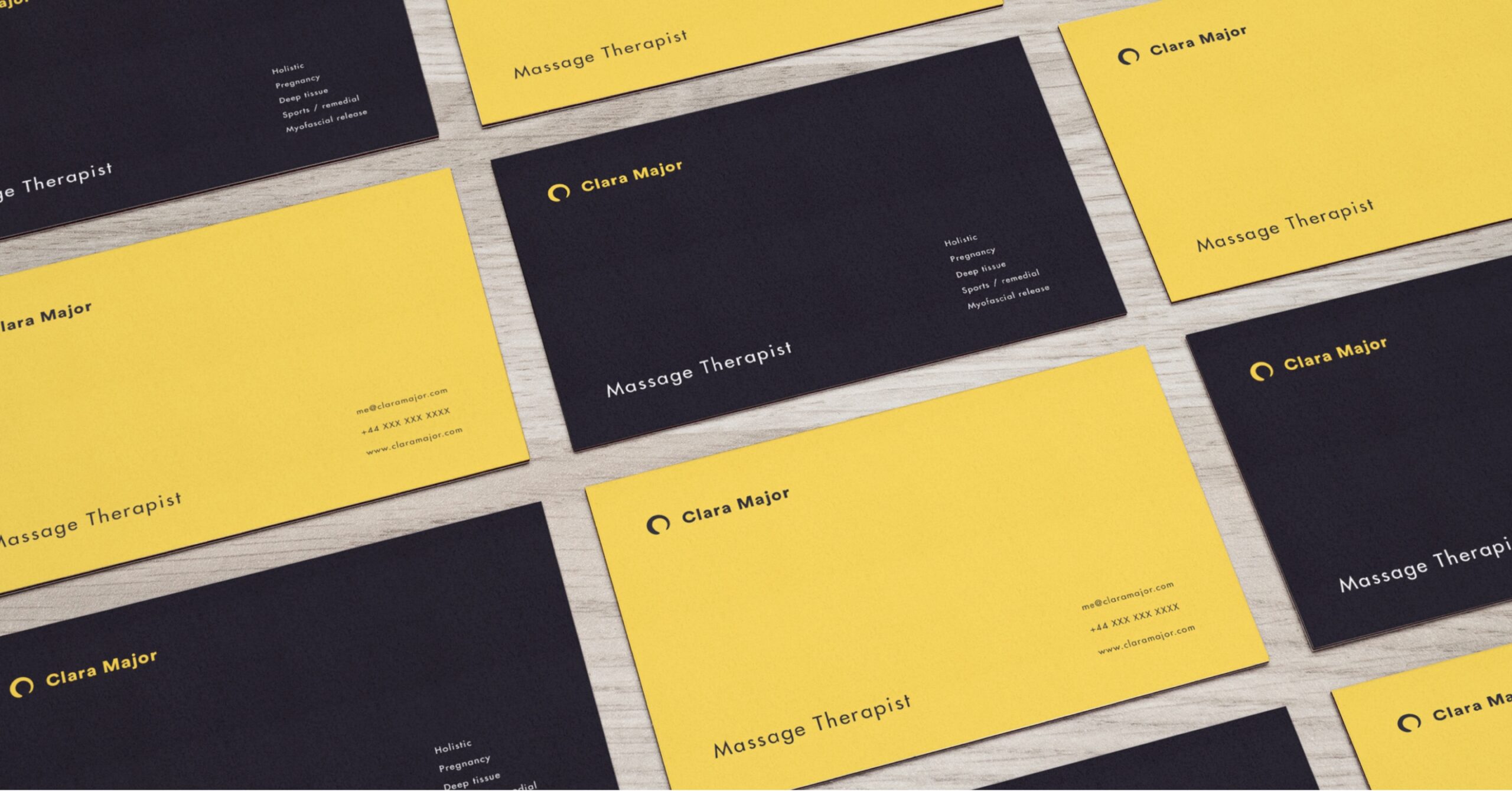 Clara major business cards laying on a desk, demostrating front side with a yellow background and the dark purple background on the back.