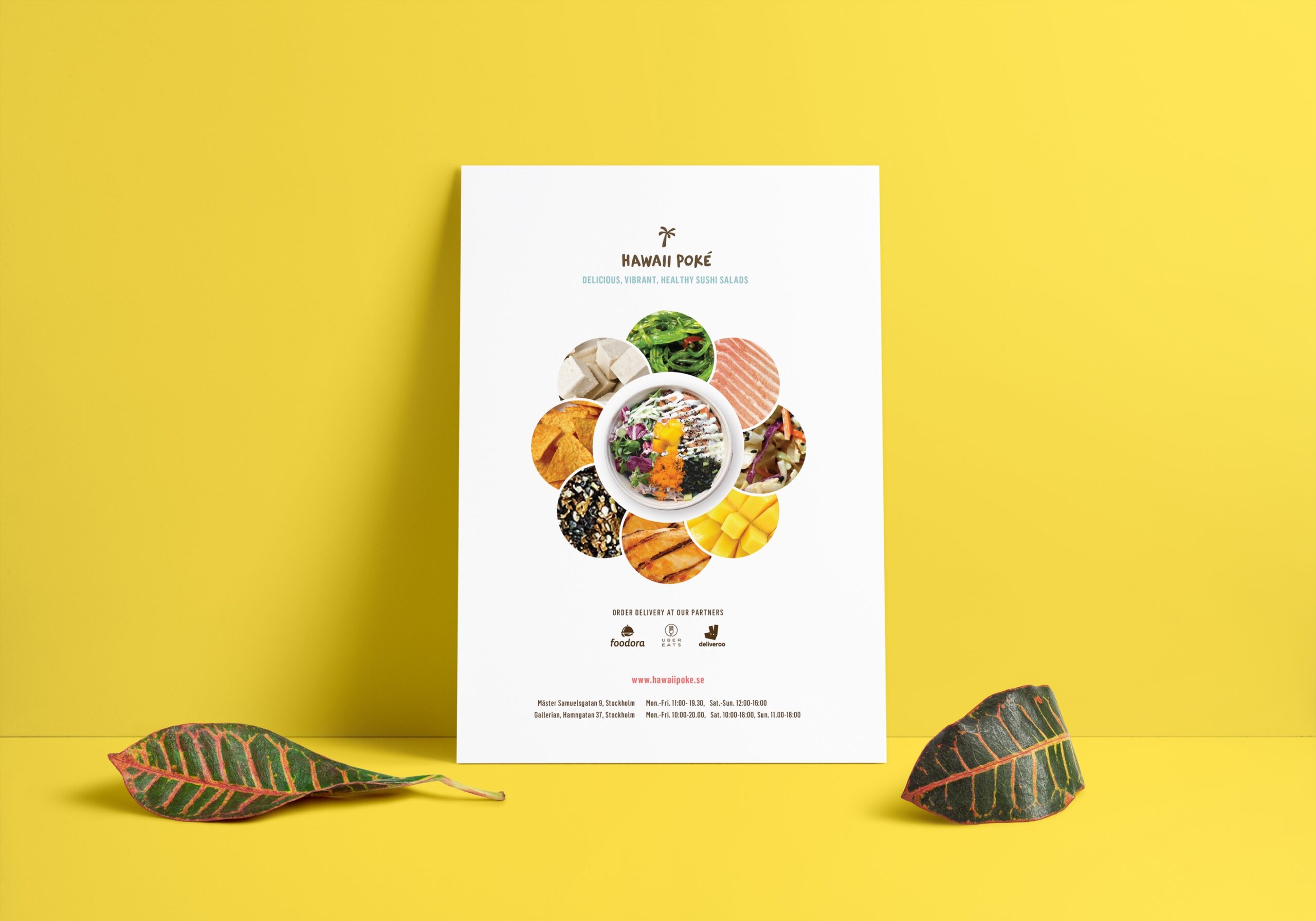 Menu flyer for a restaurant Hawaii Poke in Stockholm, leaning on a yellow wall. There two tropical leaves laying next to it