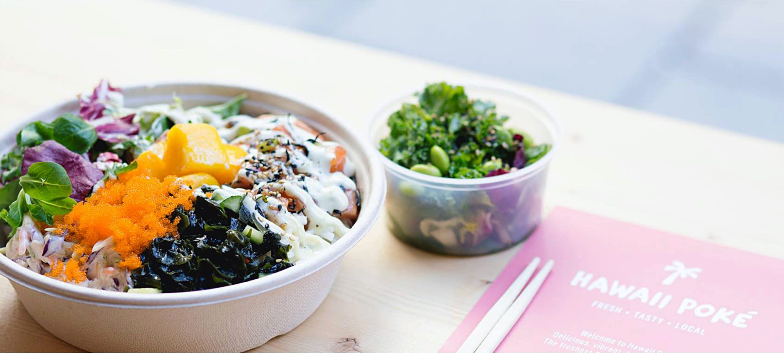 A photo from a restaurant Hawaii Poke showing a bowl with a sushi salad on the wooden bar table with chopsticks next to it